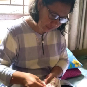 A picture of Dwi Restu embroidering her work. She is wearing glasses and a purple and white checkered shirt.