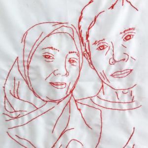 Ibu Dahlia's final embroidery of her family. It features two figures from the shoulders up, herself in a hijab and her husband. Their heads are touching and they look happy and peaceful.