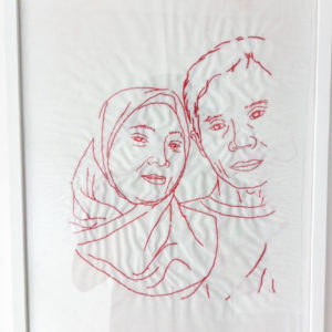Ibu Dahlia's final framed embroidery of her family. It features two figures from the shoulders up, herself in a hijab and her husband. Their heads are touching and they look happy and peaceful.